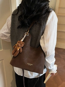 Brown minimalist tote bag with bear charm shown on model in a cozy indoor setting