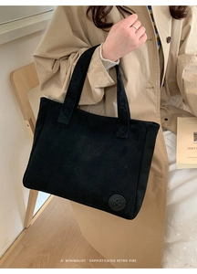 Sac cabas minimaliste en daim noir avec logo en cuir sur une chaise en bois vintage