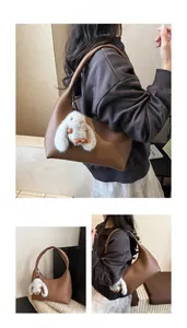 Close-up of brown pebbled leather hobo bag with a white plush bunny charm accessory