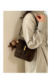 Vue latérale du sac seau en daim marron avec fermoir doré et pendentif ours au crochet