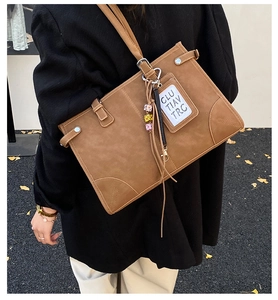 Detailed view of large brown tote bag with adjustable straps and decorative tassel charms