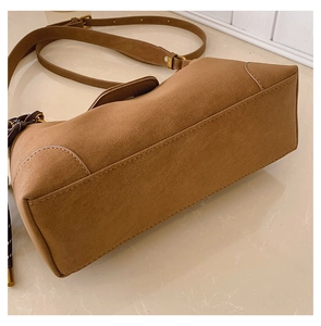 Detail view of brown matte leather handbag featuring golden metal buckle and reinforced stitching