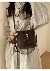 Sac seau rétro marron avec fermoir doré et ours en peluche sur une robe crème épurée