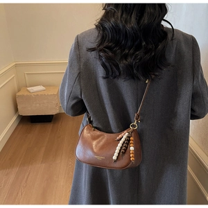 Brown leather hobo bag with ethnic style beaded pendant shown on model's shoulder
