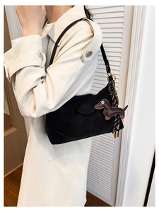 Detail of black suede shoulder bag with brown dachshund leather charm and tassel on trench coat