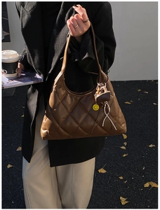 Detail of a brown quilted tote bag featuring a leather texture and a yellow smiley charm