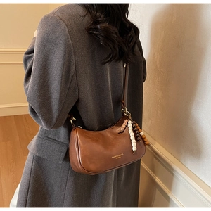 Detail of vintage brown leather crescent bag featuring wooden bead charms and long strap