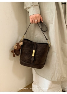 Détail d'un sac seau en daim marron foncé avec fermoir doré et charm ours tricoté