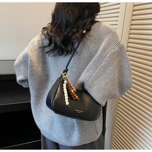 Detail of black dumpling bag with knotted shoulder strap and beaded charms on grey sweater