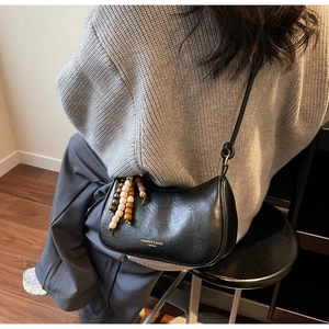 Detail of black crescent shoulder bag with wooden bead charm and knotted strap
