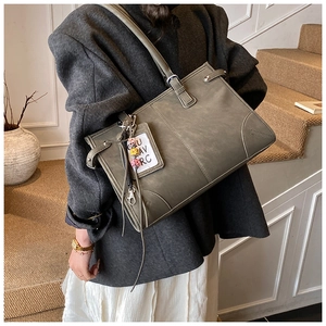 Detail of dark gray leather tote bag featuring adjustable straps and silver logo pendant
