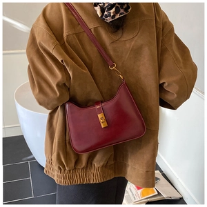 Detail of burgundy leather shoulder bag with gold metal clasp on a model