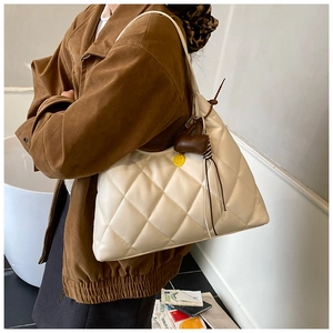 Close-up of cream quilted tote bag with bear charm detail on person's shoulder