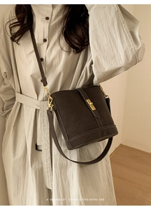 Sac seau minimaliste en cuir marron foncé avec boucle dorée sur robe chemise beige