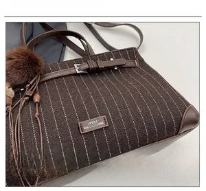 Detail of striped brown tweed handbag featuring leather straps and fuzzy pompom charm