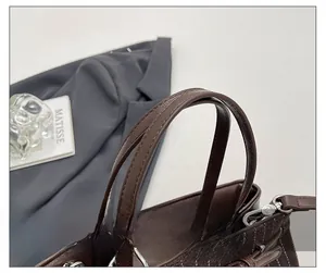 Detail of brown leather tote with vertical stripe stitching and silver metal hardware ring