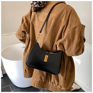 Close-up of black glossy leather underarm bag with gold metal buckle on a shoulder