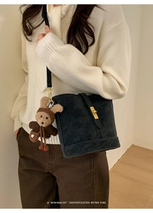 Détail d'un sac seau noir mat avec un fermoir doré et un pendentif ours en peluche mignon