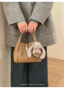 Macro shot of khaki leather handbag with silver lock and plush bunny charm detail