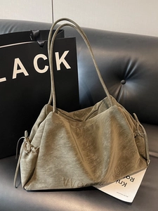 Olive green suede tote bag with side bow detail and embossed logo on black leather sofa