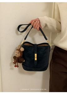 Détail d'un sac seau en daim bleu marine avec fermoir doré et breloque ours en peluche