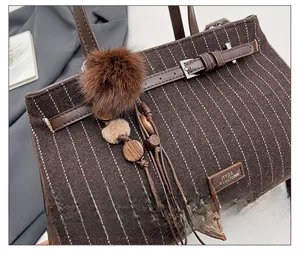 Close-up of striped wool tote bag featuring a plush fur ball and wooden bead charm
