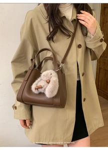 Detail of dark brown lychee leather tote bag featuring a cute beige plush rabbit charm