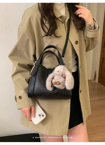 Detail of black lychee texture handbag with cute plush bunny charm and top handle