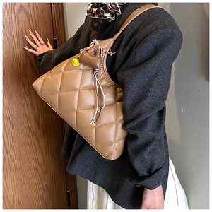 Detail of brown quilted leather tote bag with a heart charm and yellow smiley face pin