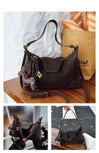 Detail of coffee brown suede crossbody bag featuring a dog charm and woven tassel