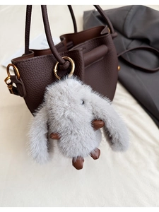 Detailed view of grey plush rabbit pendant with brown leather accents on leather bucket bag