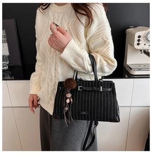 Close-up of black striped tote bag with leather buckle and soft pompom tassel accessory
