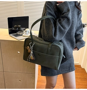 Detail of dark green matte leather tote bag with contrast stitching and pompom charm