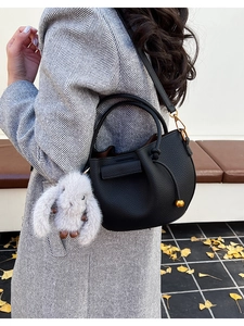 Detail of black pebbled leather bucket bag with cute plush rabbit charm on a grey coat