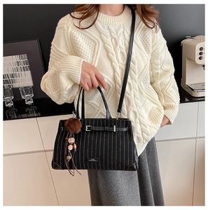 Detail of black striped tote bag featuring a decorative pompom charm and metal logo plate