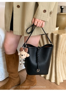 Detail of black lychee leather bucket bag with plush bear charm and beaded handle