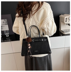Detail of black striped crossbody bag with brown fur pom-pom charm and leather handle