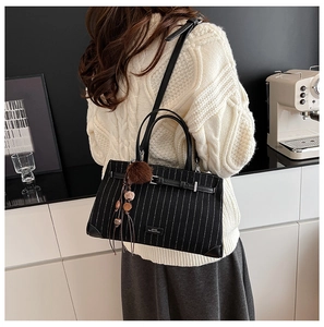 Detail of striped tote bag with leather strap and decorative pompom charms on model