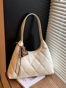 Chic beige quilted hobo bag with heart charm and woven strap on a wooden table