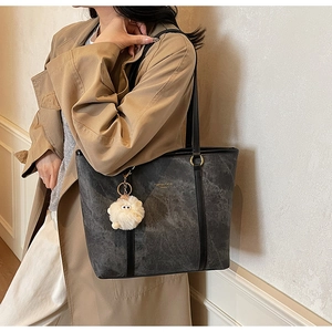 Detail of dark grey marble tote bag with plush charm and gold hardware on trench coat
