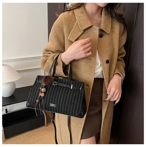 Detail of striped tote bag with leather strap buckle and fuzzy charm on wool coat