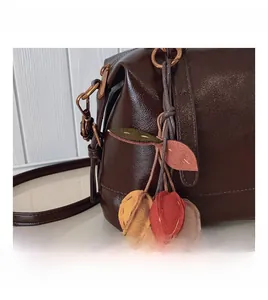 Detail der dunkelbraunen Lederhandtasche mit bunten Taschenanhängern in Blatt- und Fruchtform