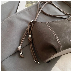 Detail of dark brown suede shoulder bag featuring contrast stitching and silver metal beads