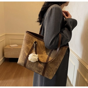 Close-up of marble texture brown suede tote bag with contrast leather strap and pom-pom