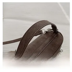 Détail d'un sac à main marron foncé en cuir grainé avec larges anses et boucles métalliques