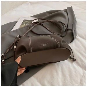 Close-up of dark brown leather handbag with contrast white stitching and side drawstrings