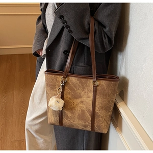 Close-up of brown textured tote bag with FOR YOUNG 1989 text and a plush sheep charm