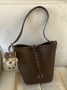 Brown litchi grain bucket bag with a plush bear charm on a vintage book background