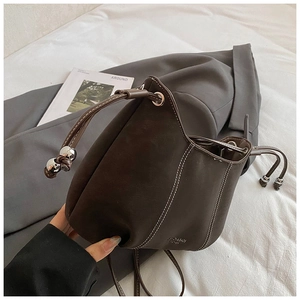 Detail of dark brown leather bucket bag with white contrast stitching and drawstring