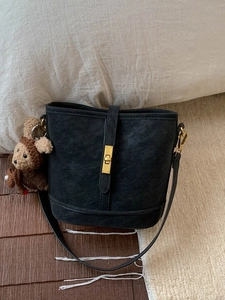 Sac seau rétro en cuir noir avec fermoir doré et charme d'ours dans un décor cosy